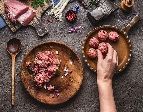 Meat balls making. Female hand puts meat ball in frying pan. Preparation on kitchen table with meat, force meat , meat grinder and spoon, top view. Cooking,recipes and eating concept