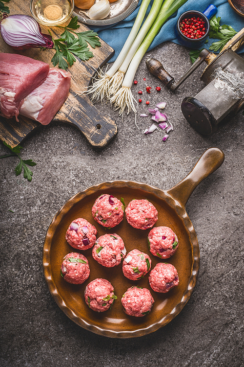 Raw meat balls in frying pan on rustic background with ingredients and kitchen tools, top view. Force meat recipes