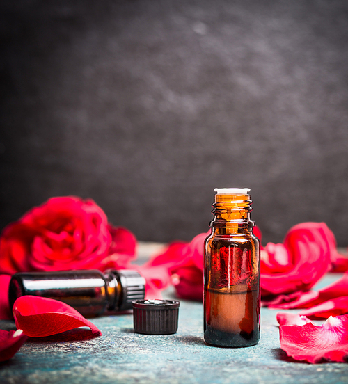 Bottle of roses essential oil and petals of red roses , side view, close up