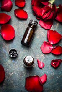 Roses essential oil with red roses petals on rustic background. Cosmetic , aromatherapy , spa or wellness concept.