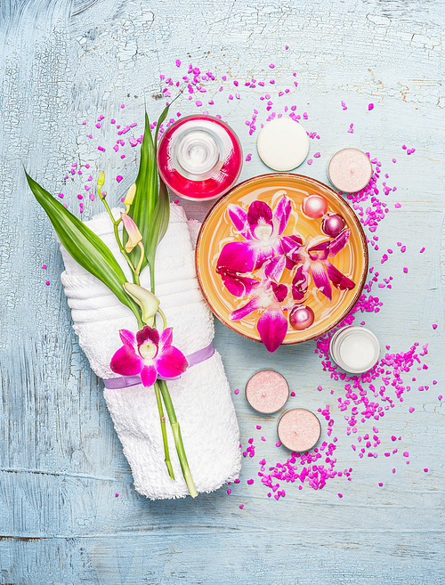 spa or wellness setting with towel, bamboo leaves ,  bowl with pink orchid flowers and  water , cream, candles and 씨솔트 on light blue  shabby  rustic background, top view