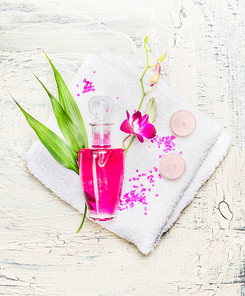 Elegant bottle of lotion , pink orchid flowers and  green bamboo leaves on white towel on light wooden background, top view. Spa, wellness or body care concept