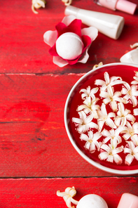 Red bowl with white flowers in water, bottle with  lotion on wooden table , spa background,  top view