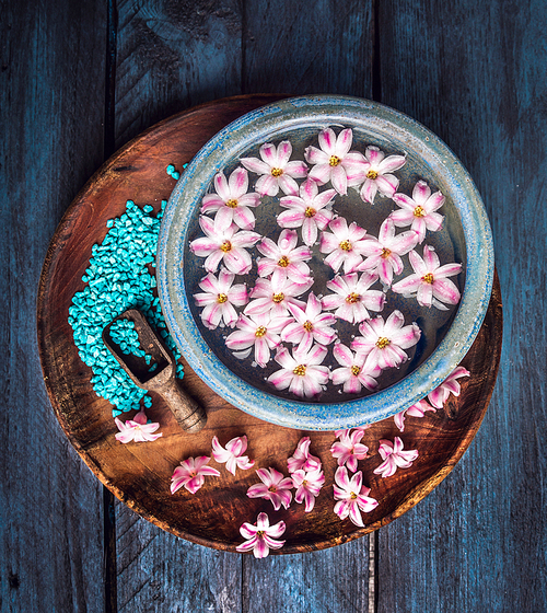 water bowl with flowers and scoop with 씨솔트 on blue wooden background, top view