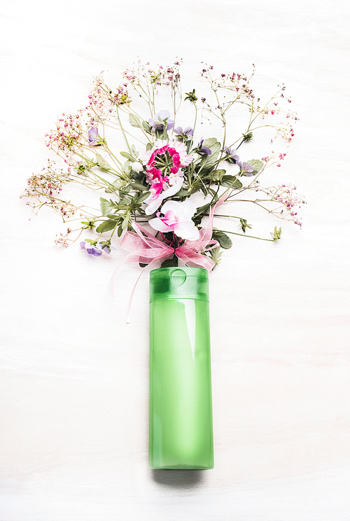 Green Vial with  organic botanical cosmetic product and flowers and herbs bunch on white wooden background, top view. Organic herbal and  botanical cosmetic,  beauty and skincare product concept