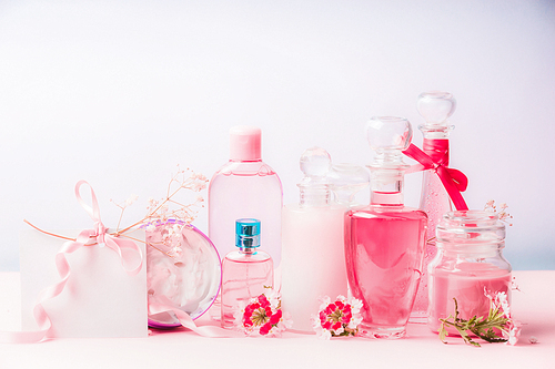 Various natural cosmetic products in bottles and jars with pink flowers at pastel background, front view. Beauty and skin care concept on pastel background, front view