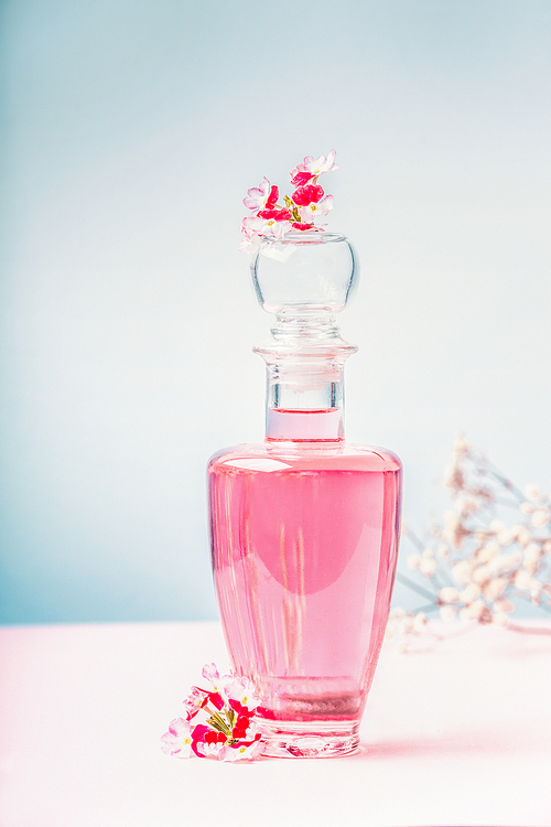 Bottle of lotion or perfume with pink flowers , natural cosmetic product or beauty concept on pastel blue background, front view