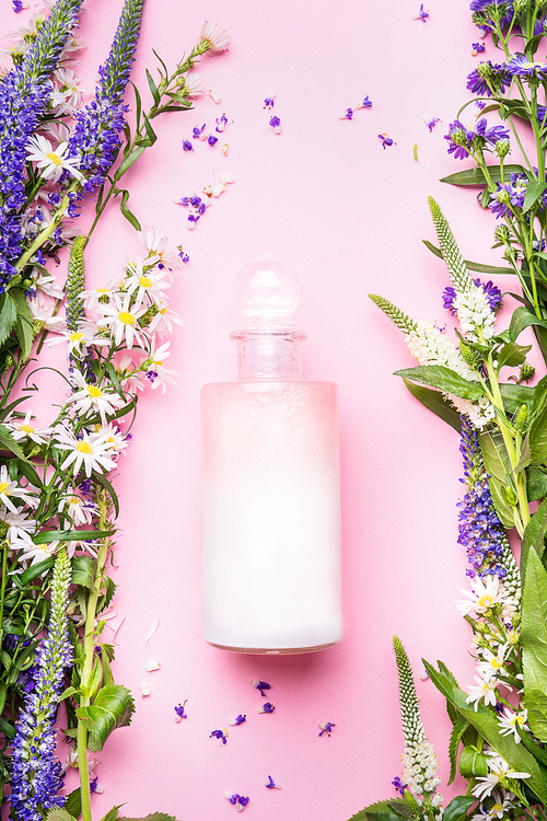 Natural cosmetic product bottle of lotion,shampoo or moisturizer with herbs and flowers on pink background, top view, copy space, vertical. Beauty, skin and hair care concept
