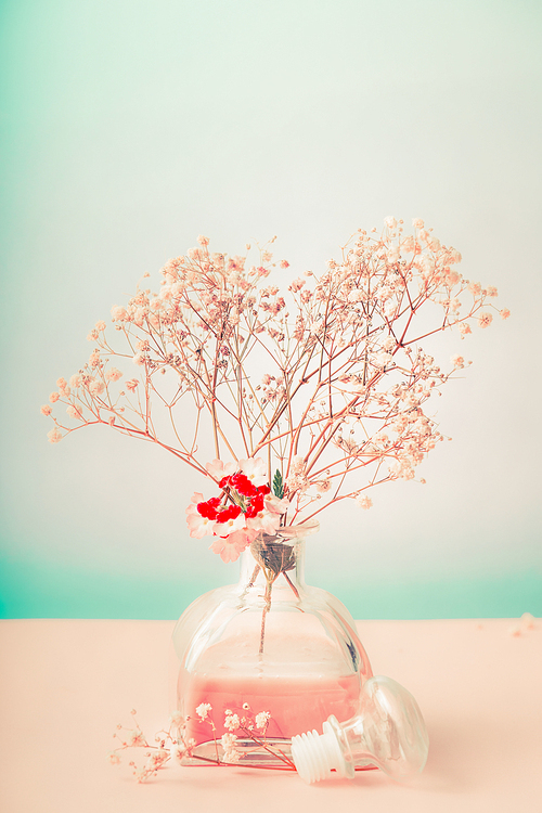 Bottle with room fragrance and flowers on pastel background, front view