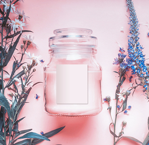 Natural cosmetics jar with pastel pink cream or peeling , herbal leaves and wild flowers, blank label for branding mock-up on pastel background, top view