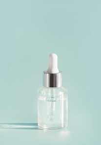 Cosmetic transparent liquid in glass bottle with dropper. Serum skin care product on light mint background, front view with copy space. Beauty product concept. Blank label for branding mock-up