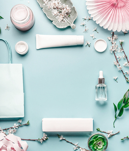 Beauty background with facial cosmetic products, shopping bag and twigs with cherry blossom on pastel blue desktop background. Spring skin care trends, top view, frame, flat lay. Branding mock up