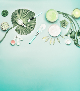 Natural cosmetic background. Tools and accessories for home facial skin care with flowers and green tropical leaves, top view, flat lay. Serum,  face mask and candle on turquoise background.