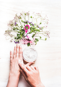 Female hands apply cream on skin on white background with plants and flowers , top view. Natural cosmetic concept
