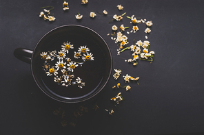 Cup of chamomile tea on dark background, top view with copy space for your design. Healthy tea ingredients and  home remedy for cosmetic treatment. Herbal medicine concept