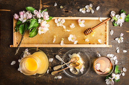 honeycomb with wooden dipper and fresh blossom,  jar with honey and plate with vintage spoons on dark rustic background, top view