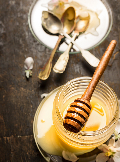 Honey dipper on  glass jar and plate with vintage spoons on rustic wooden background, close up