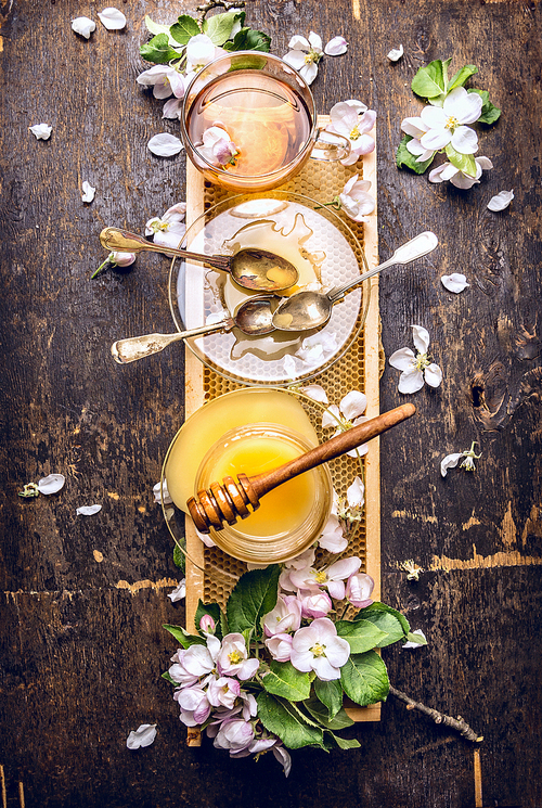 Honey, tea and spring blossom on honeycomb, dark wooden background, top view