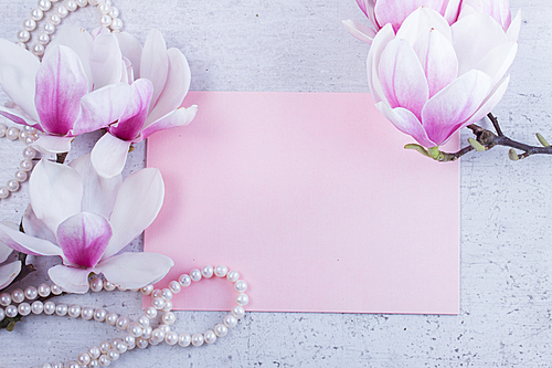 Magnolia flowers and jewellery flat lay composition with copy space on pink paper invitation