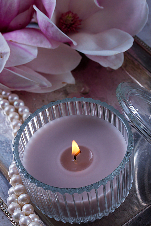 burning candle and magnolia fresh flowers on tray