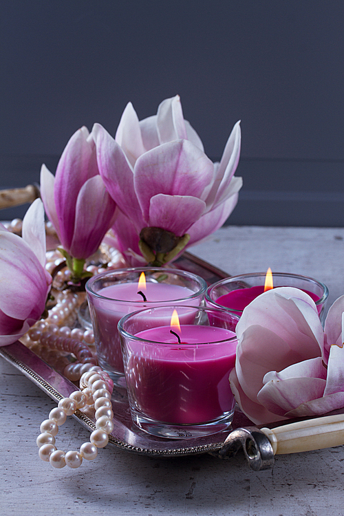 Gray room interior decor with burning candle and magnolia flowers on desk