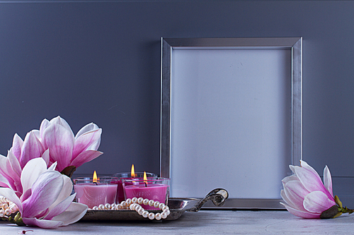 Gray room interior decor with magnolia flowers, burning hand-made candle and poster mock up