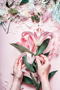Female hands making lovely pink lily flowers bouquet on pastel  table with florist decoration equipment, top view. Creative Florist workspace and flowers arrangement.  Festive holiday concept.