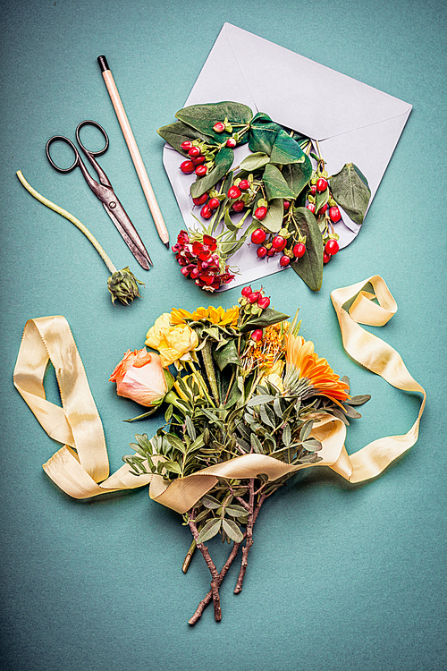 Autumn flowers bunch with envelop , shears , pencil and flowers on blue workspace table background, top view. Creative Flowers arrangement.  Invitation , greeting and holiday, concept