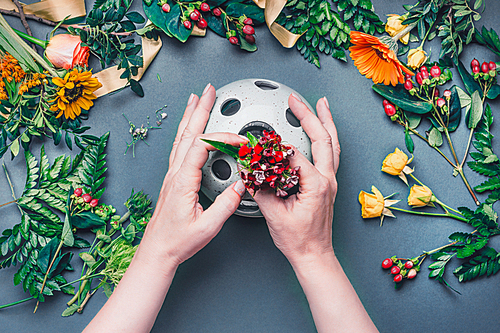 Female hands make Creative autumn floral arrangement with various flowers and plant leaves arrangement on blue table , top view. Florist workplace. Greeting and holiday, concept