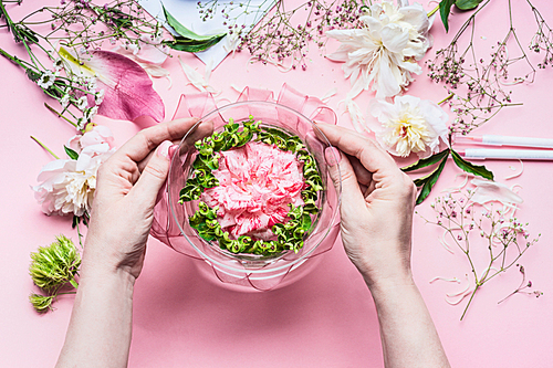 Pink Florist workspace with Lilies and other flowers, glass vase with water. Female hands making  Festive Flowers arrangements , top view
