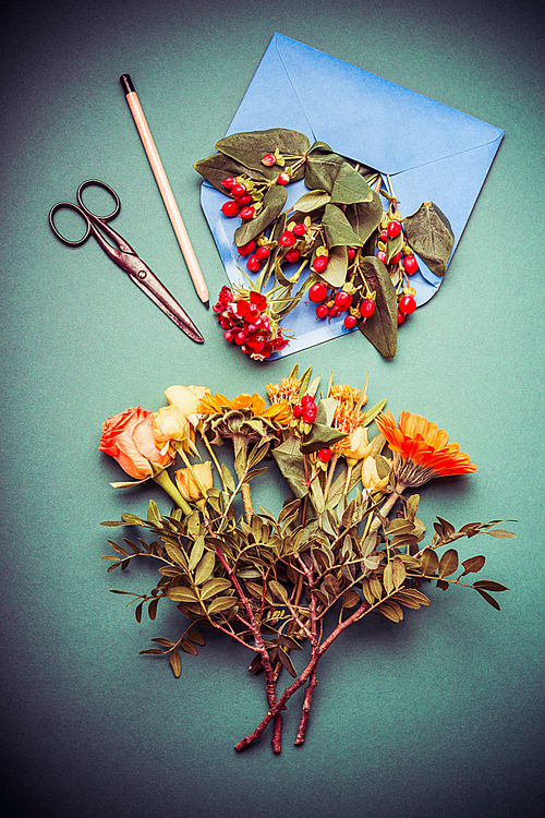 Autumn  flowers arrangements making on table workspace with scissors , envelope and ribbon, top view
