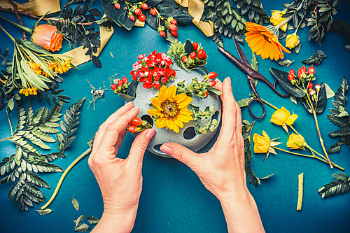 Female hand making autumn flowers  arrangements at blue florist workspace background, top view