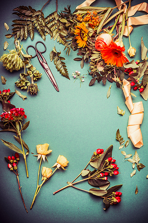 Autumn flowers on florist table with ribbon and scissors on blue background, top view, frame. Autumn Bouquet making preparation