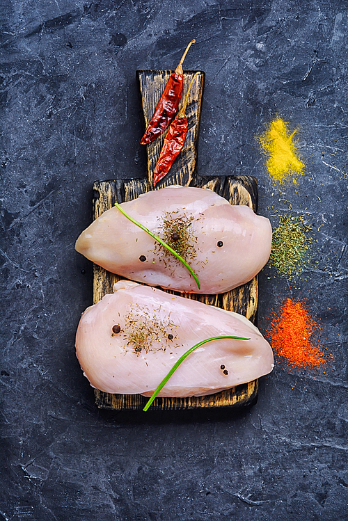 chicken raw fillets on kitchen wooden board with spices and onions