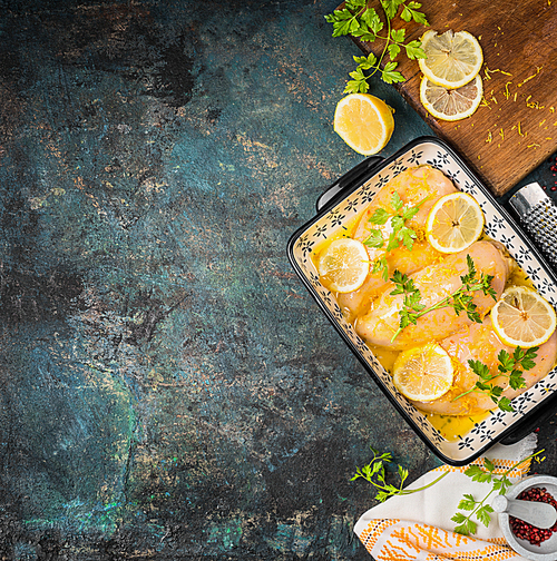 Lemon Chicken in baking dish. Chicken breast Cooking ingredients, lemon and butter sauce on dark rustic background , top view, border