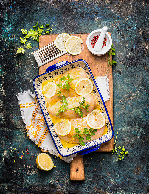 Lemon Chicken in baking dish with ingredients on wooden cutting board and rustic background, top view