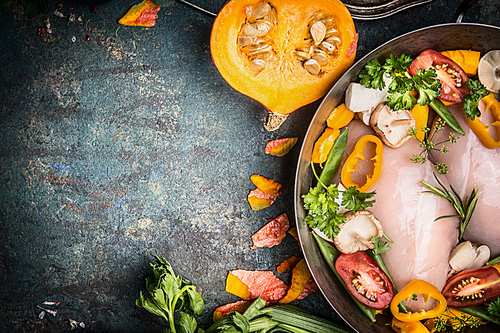 Raw chicken breast in cooking pot with pumpkin and vegetables ingredients on dark rustic background, top view, place for text