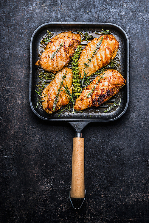 Roasted chicken breast in grill pan with fresh herbs and spices  on dark rustic background, top view