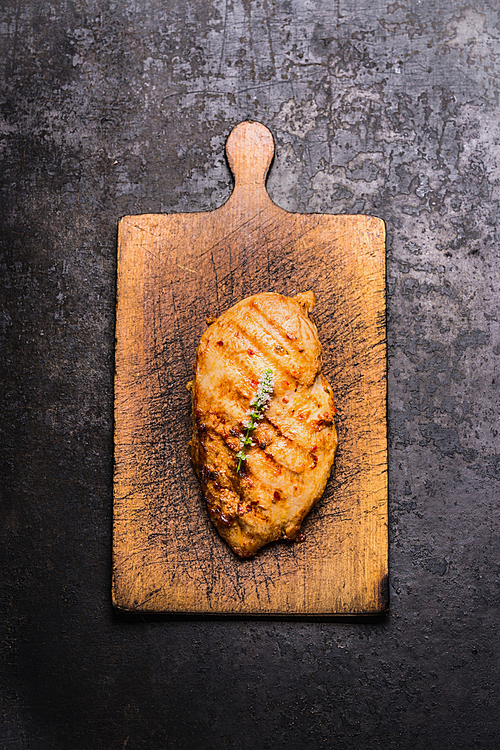 Roasted chicken breast on wooden cutting board on dark rustic background, top view