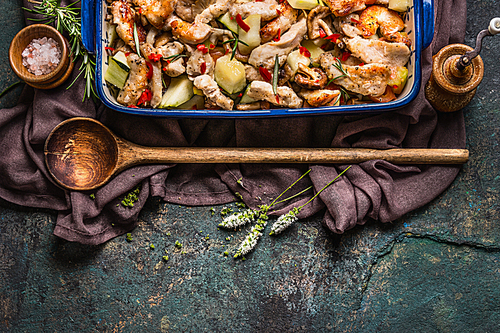 Roasted Chicken with vegetables in casserole with wooden spoon and fresh herbs on dark rustic background, top view, border