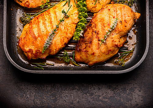 Roasted chicken breast in frying pan with herbs, top view, close up