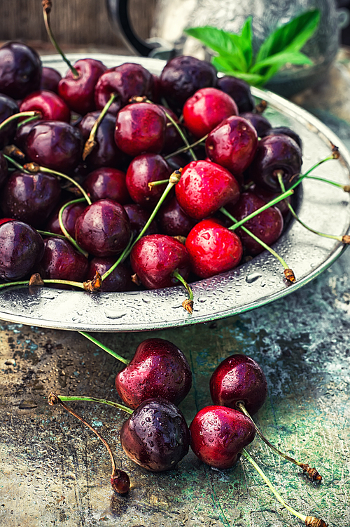 ripe large cherries in the iron bowl iron on the background in bright sunlight.The image is tinted.Selective focus