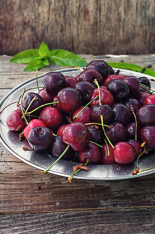 Ripe cherries on wooden background in the iron bowl