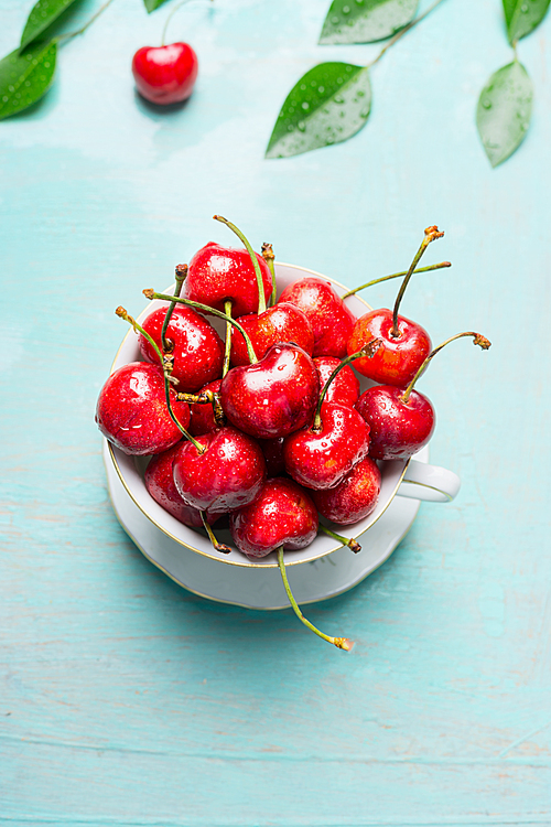 Old cup with sweet cherries on blue background, top view. Summer fruits and berries concept.