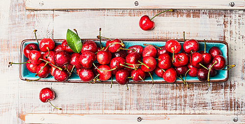 Blue bowl with sweet cherry harvest  on light wooden background, top view