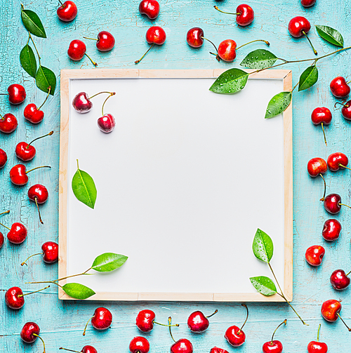 Lovely ripe sweet cherry with leaves around blank white chalkboard, top view. Berries background