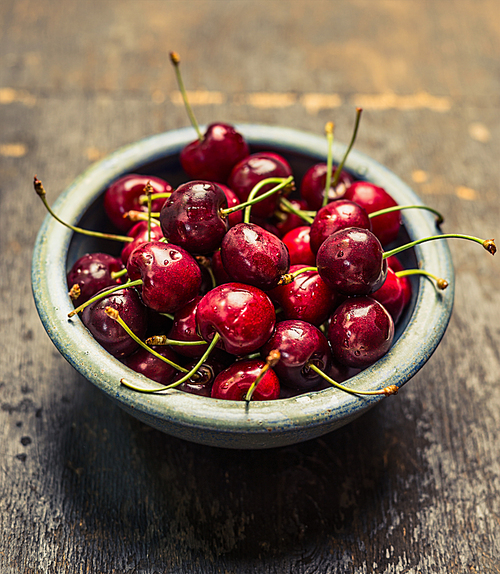 Blue bowl with sweet cherries on rustic wooden background