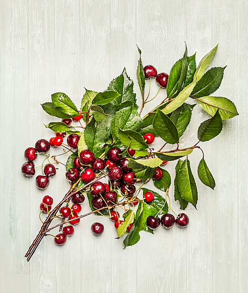 Ripe cherry branch with fruits and green leaves on wooden background, top view