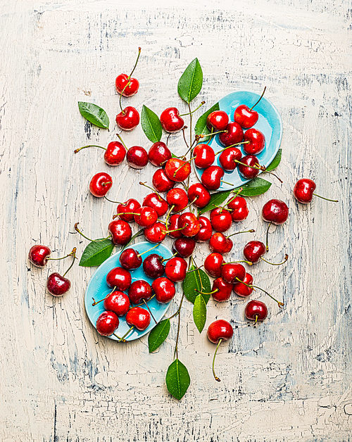 Tasty red cherries with leaves in blue bowls and table, top view composing. Summer fruit  and berries concept