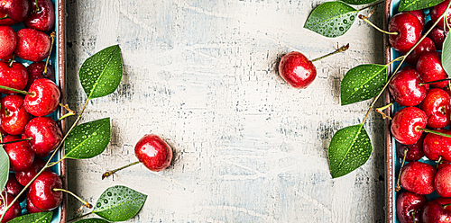 Red sweet cherries background with green leaves on white wooden vintage background, top view, frame